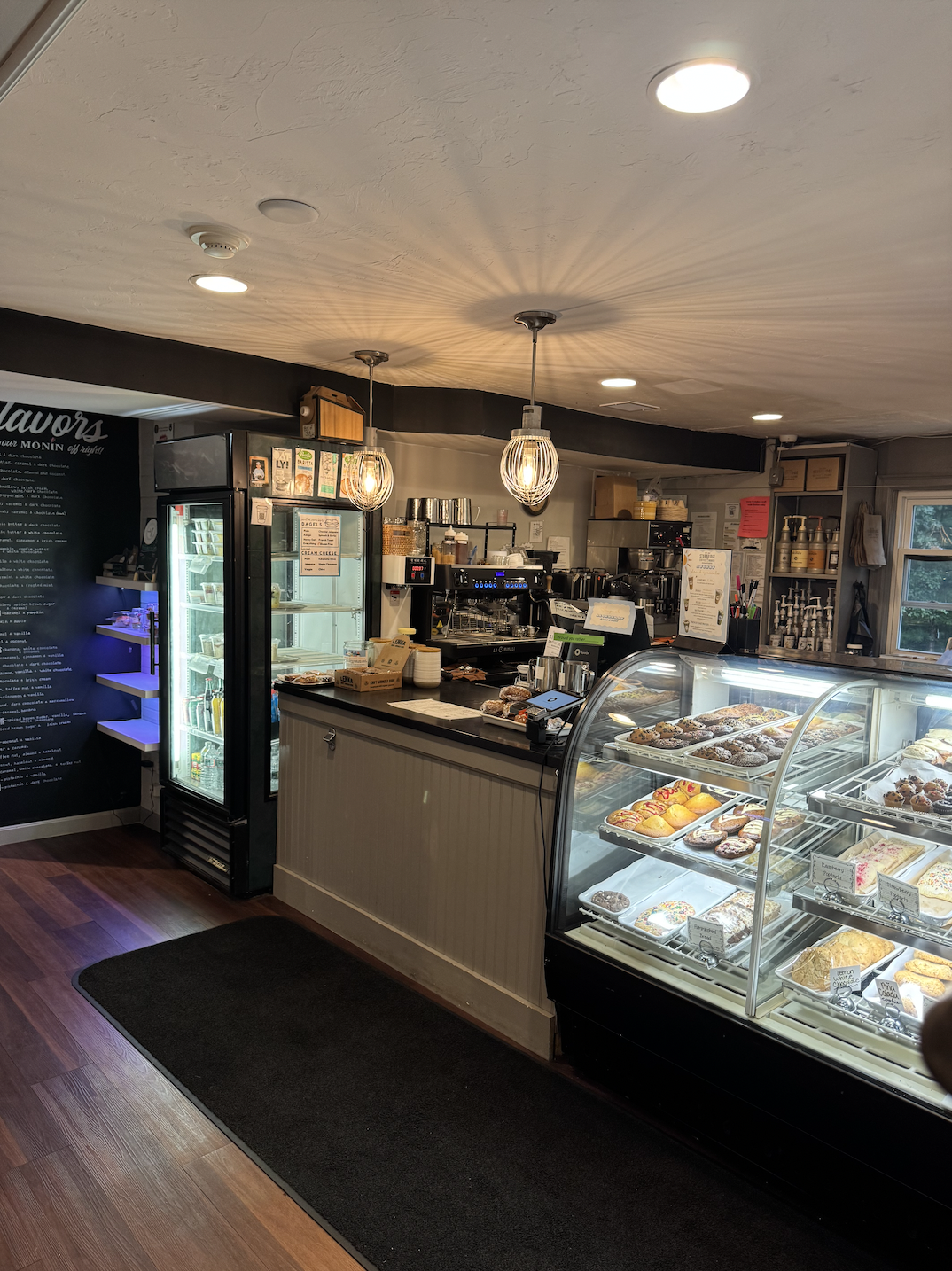 Inside a coffee shop with a refrigerator, a counter, and a baked goods case 