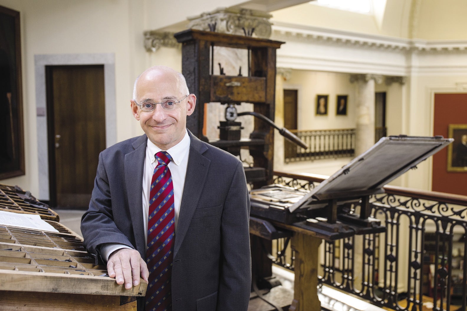 A man stands in a suit in front of an old printing press