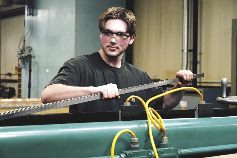 A young man wears safety glasses while operating a manufacturing machine with yellow wiring.