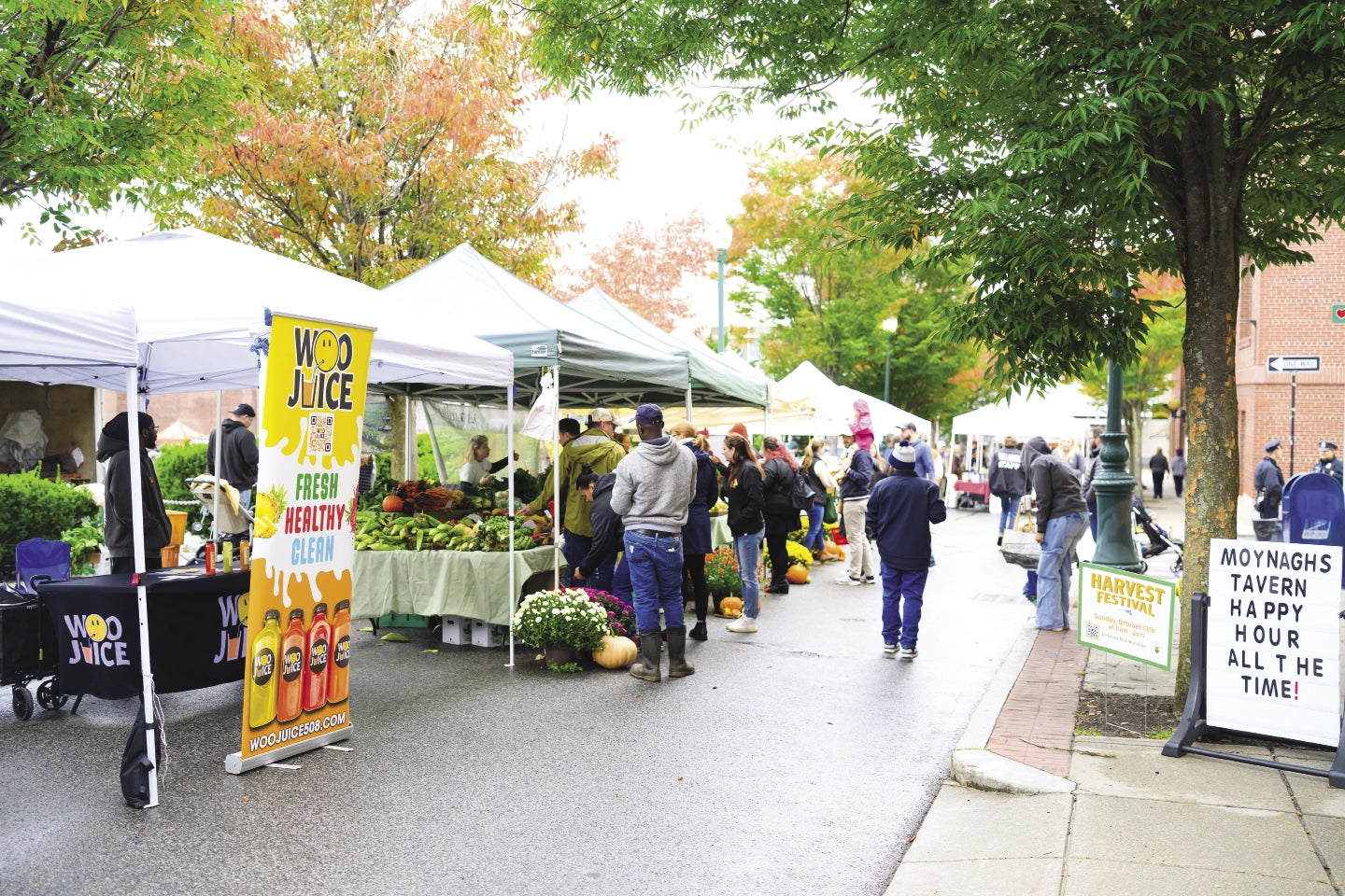 Outside a farmers market with tents over vendors selling produce and people walking down the sidewalk.
