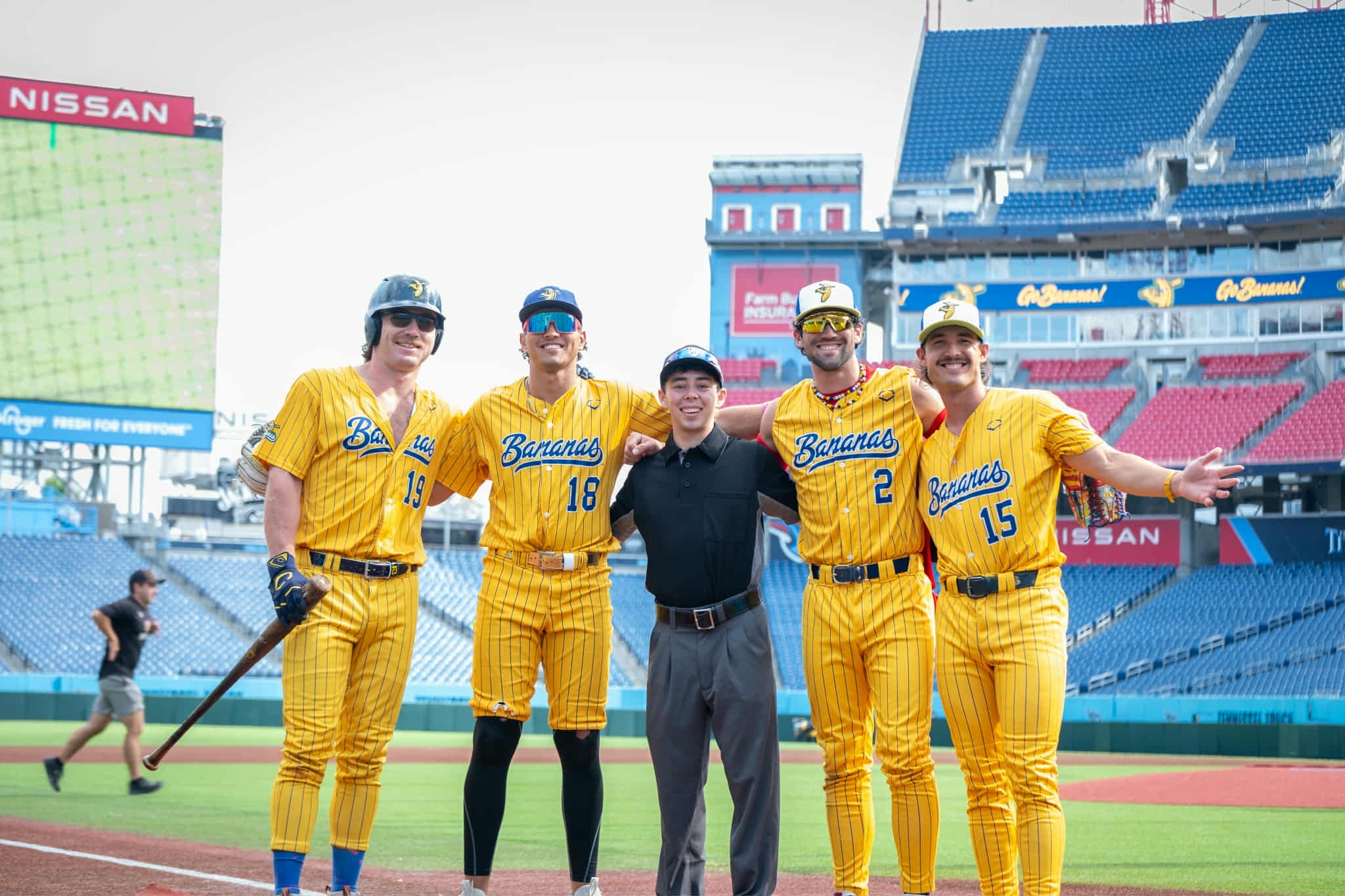 A man stands between four baseball players wearing yellow uniforms standing in the middle of a baseball stadium.