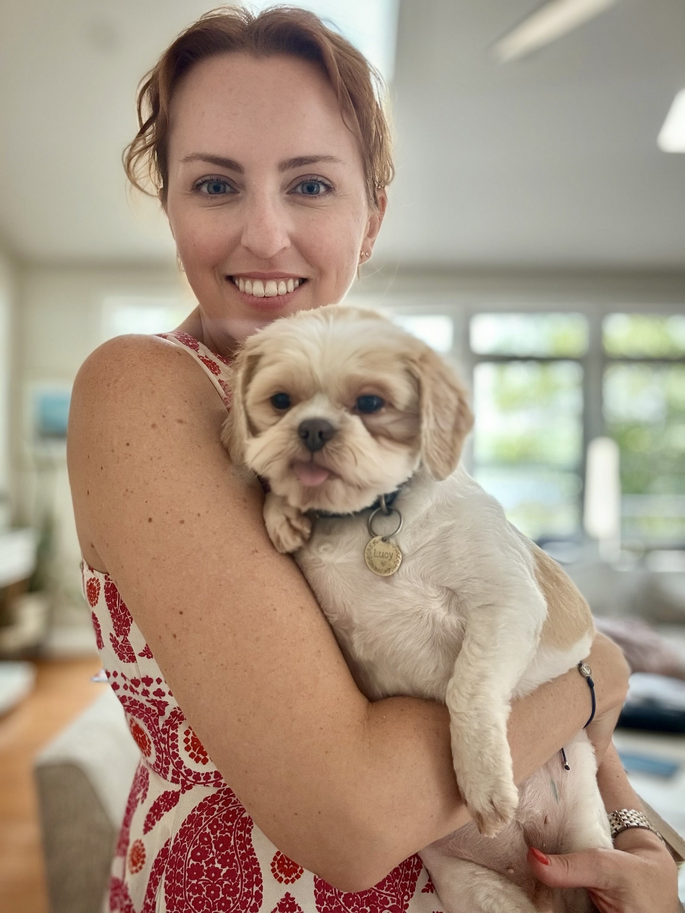 A woman wearing a red and yellow dress holds a small white dog.
