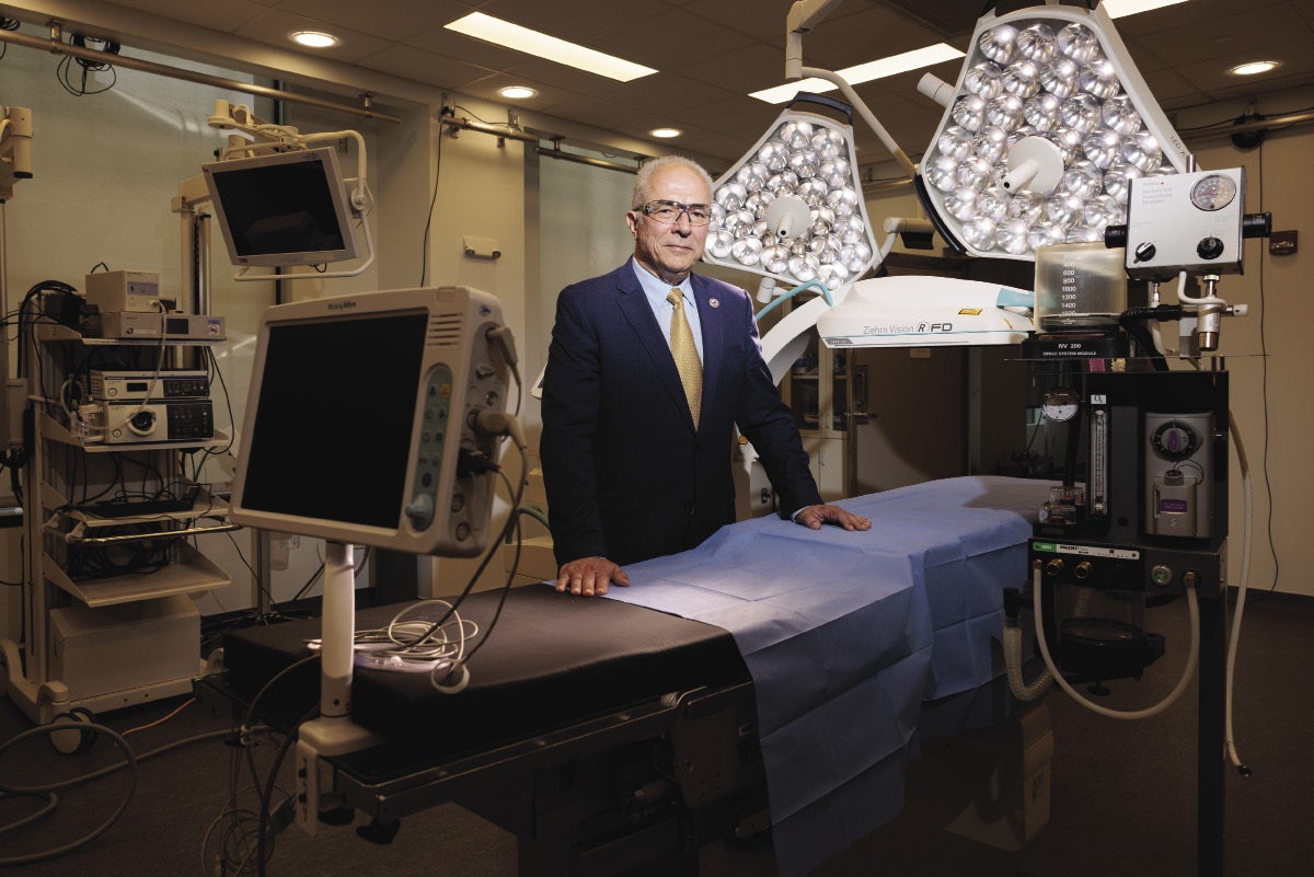 Man in suit stands in operating room with hands on the operating table