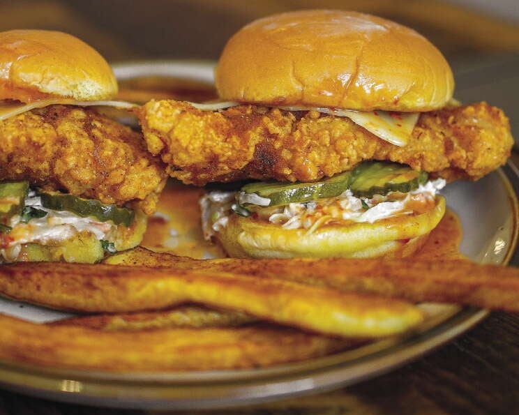 Two fried chicken sandwiches with pickles and cole slaw sit on a plate with fries.