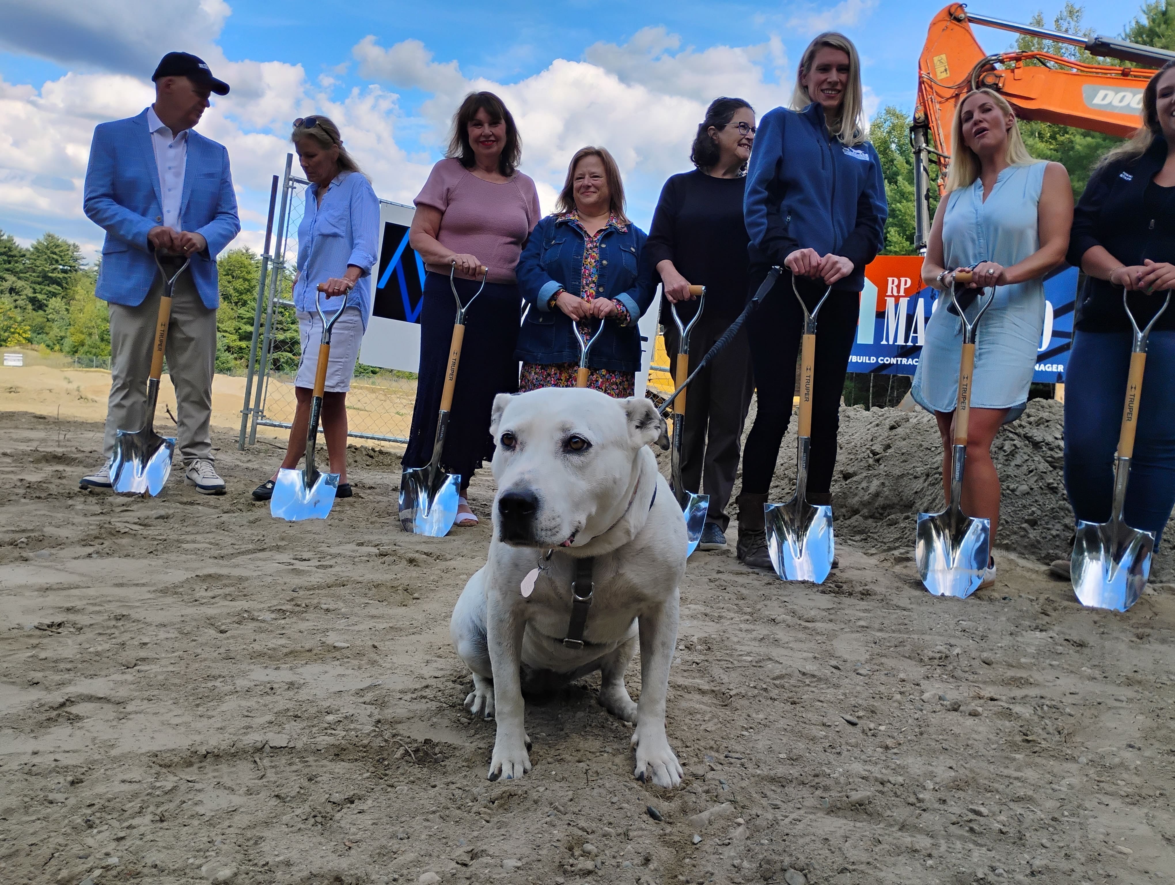 Dog sits in front of line of people holding shovels