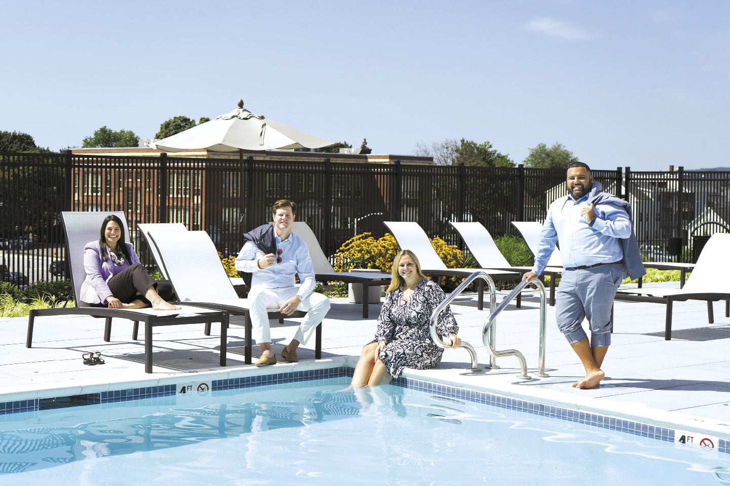Four people stand and sit around a pool outside.