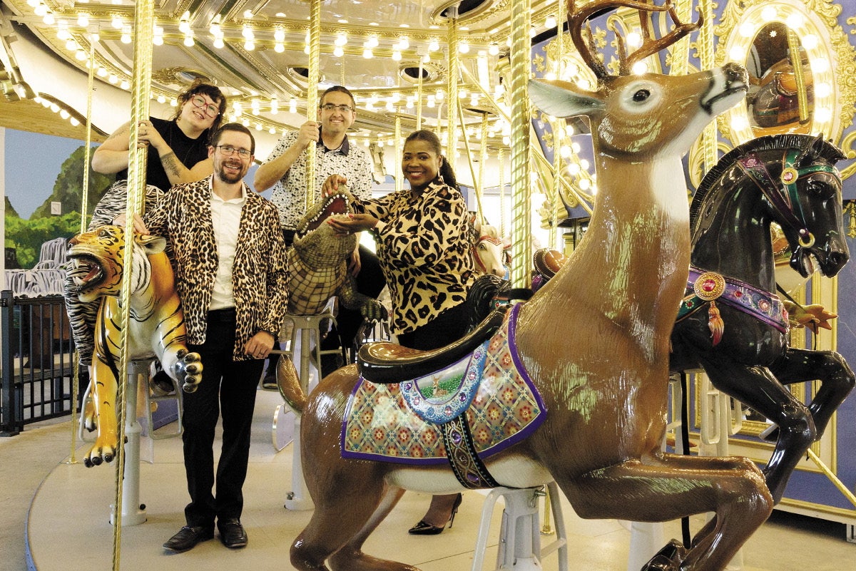 Four people on a carousel standing around and sitting on animal-shaped seats