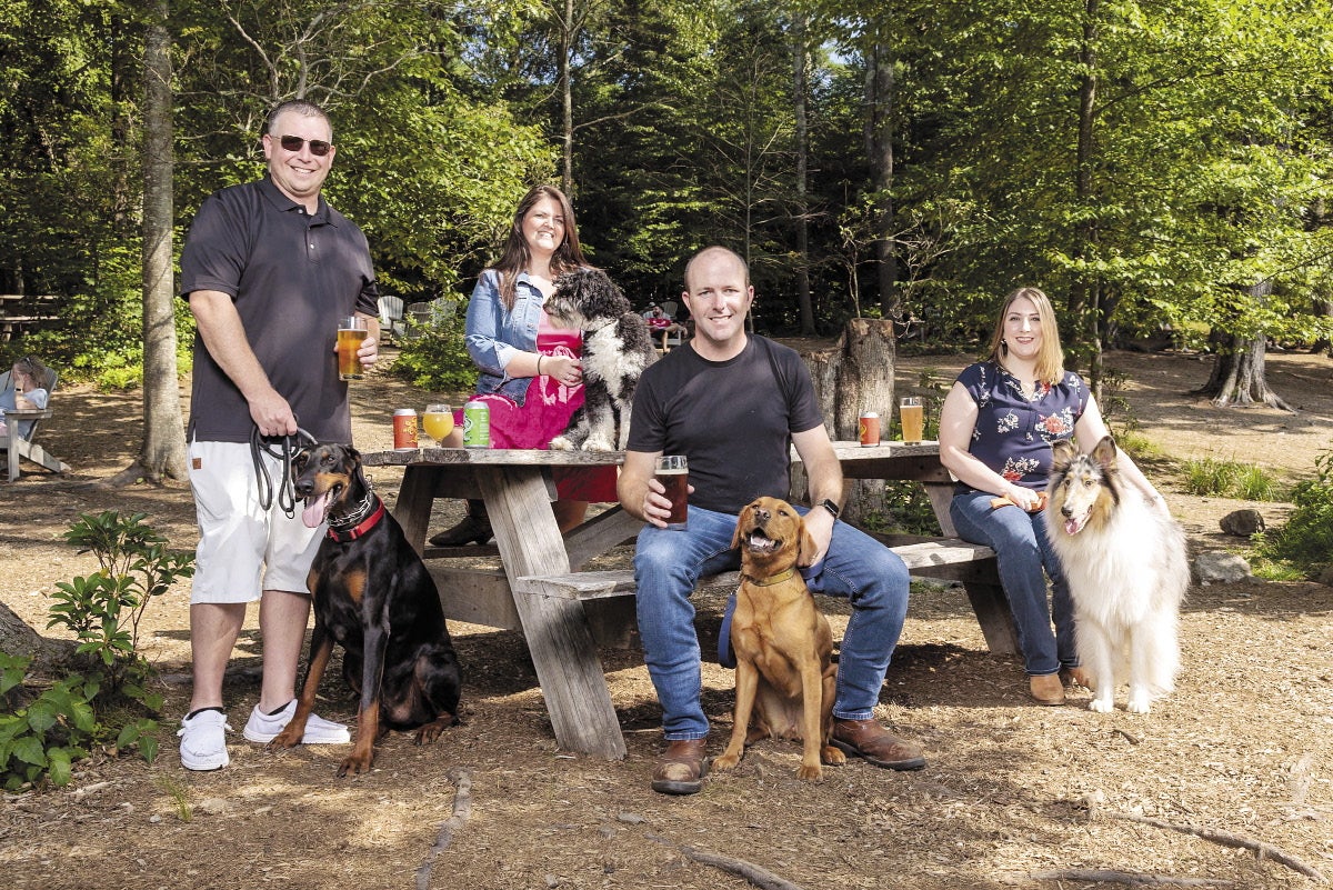Four people stand and sit around a picnic table outside with dogs.