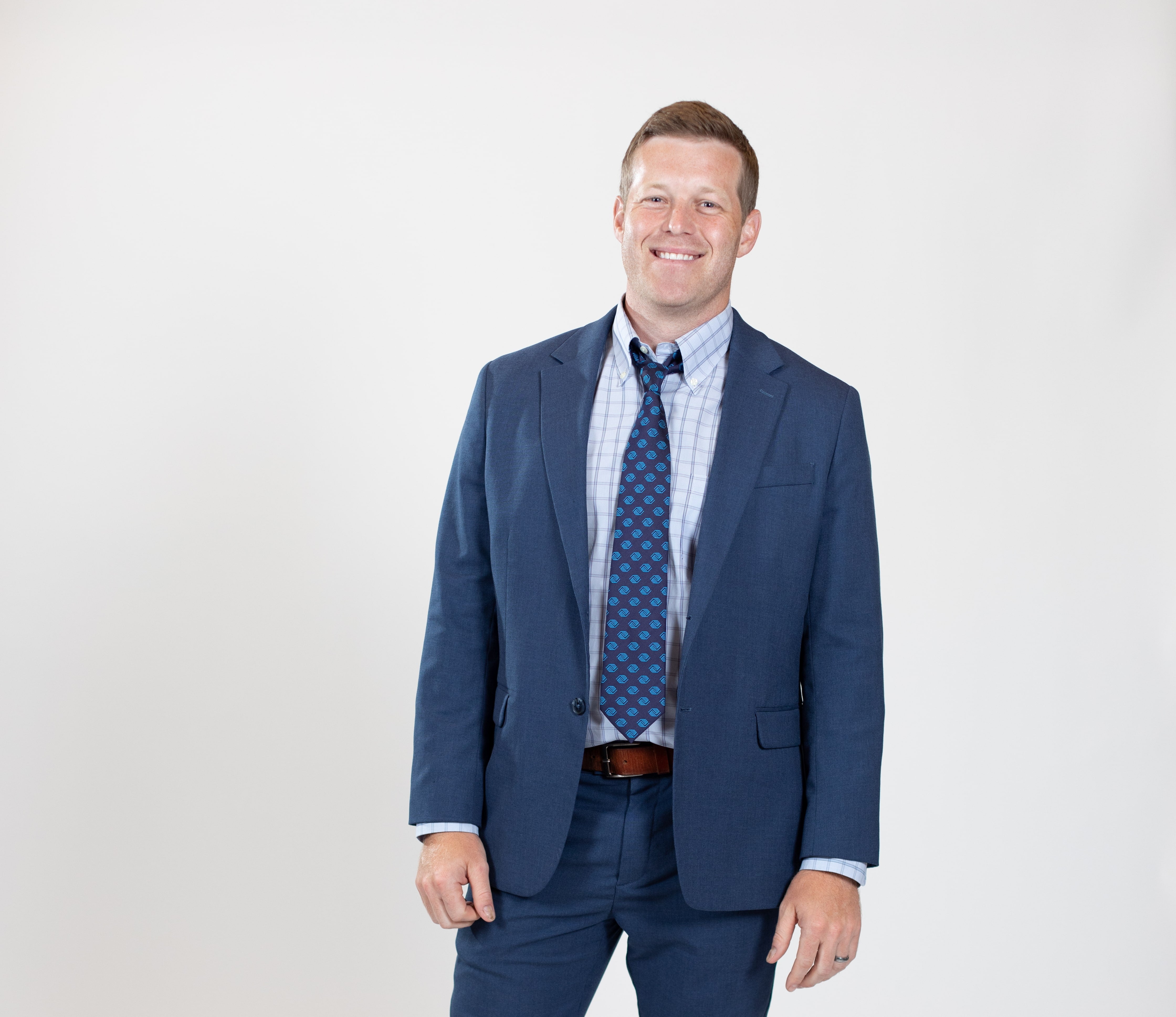 A man wears a blue suit with a blue-spotted tie.