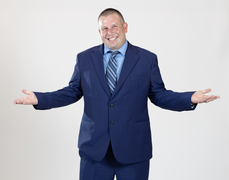 A man wearing a blue suit stands with his hands held out to his sides.