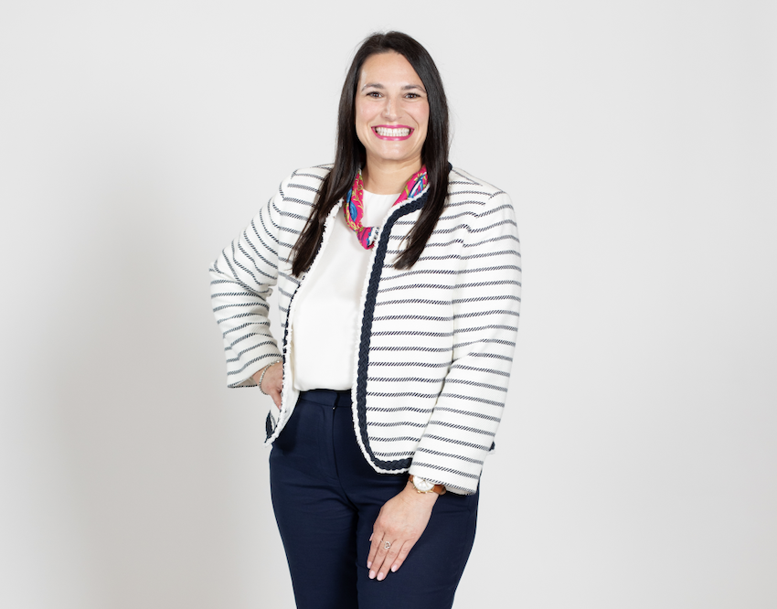 A woman with brown hair wears a white and black striped cardigan, a white blouse, and a jeans.