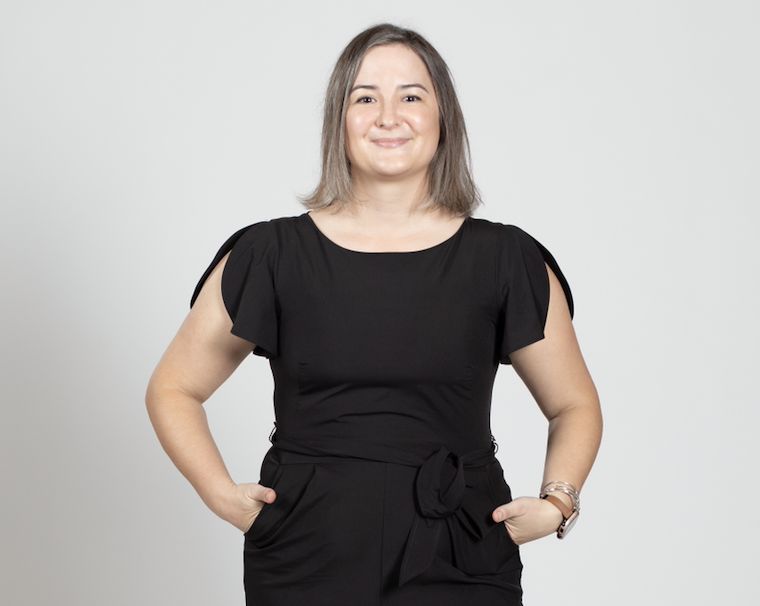 A woman wearing a black jumpsuit stands with her hands in her pockets.