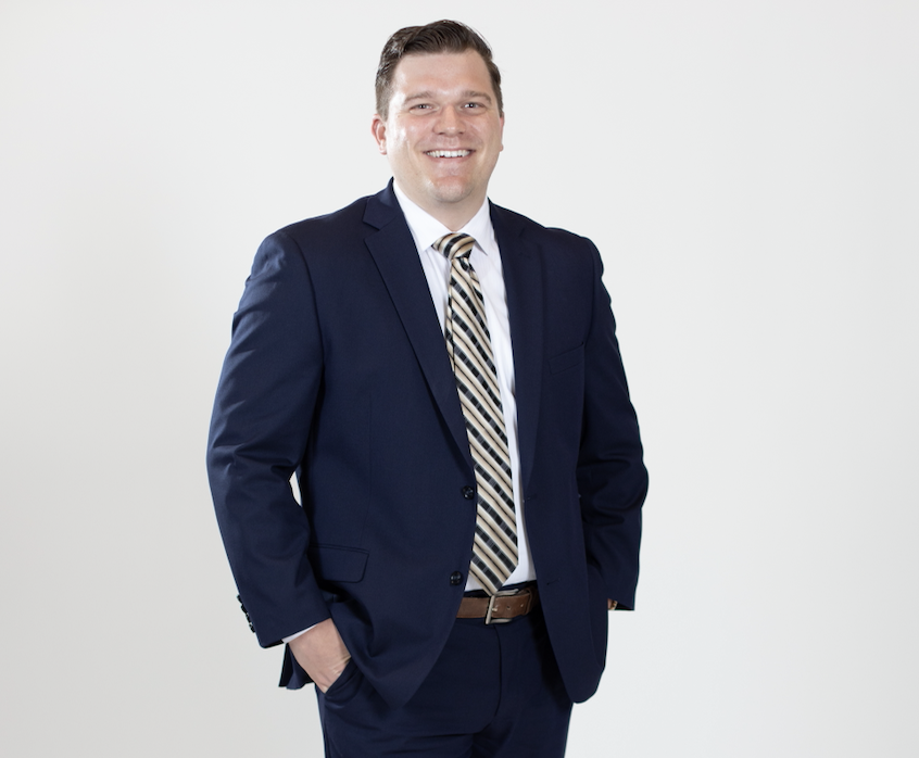 A man wearing a blue suit, white shirt, and striped tie stands with his hands in his pockets.