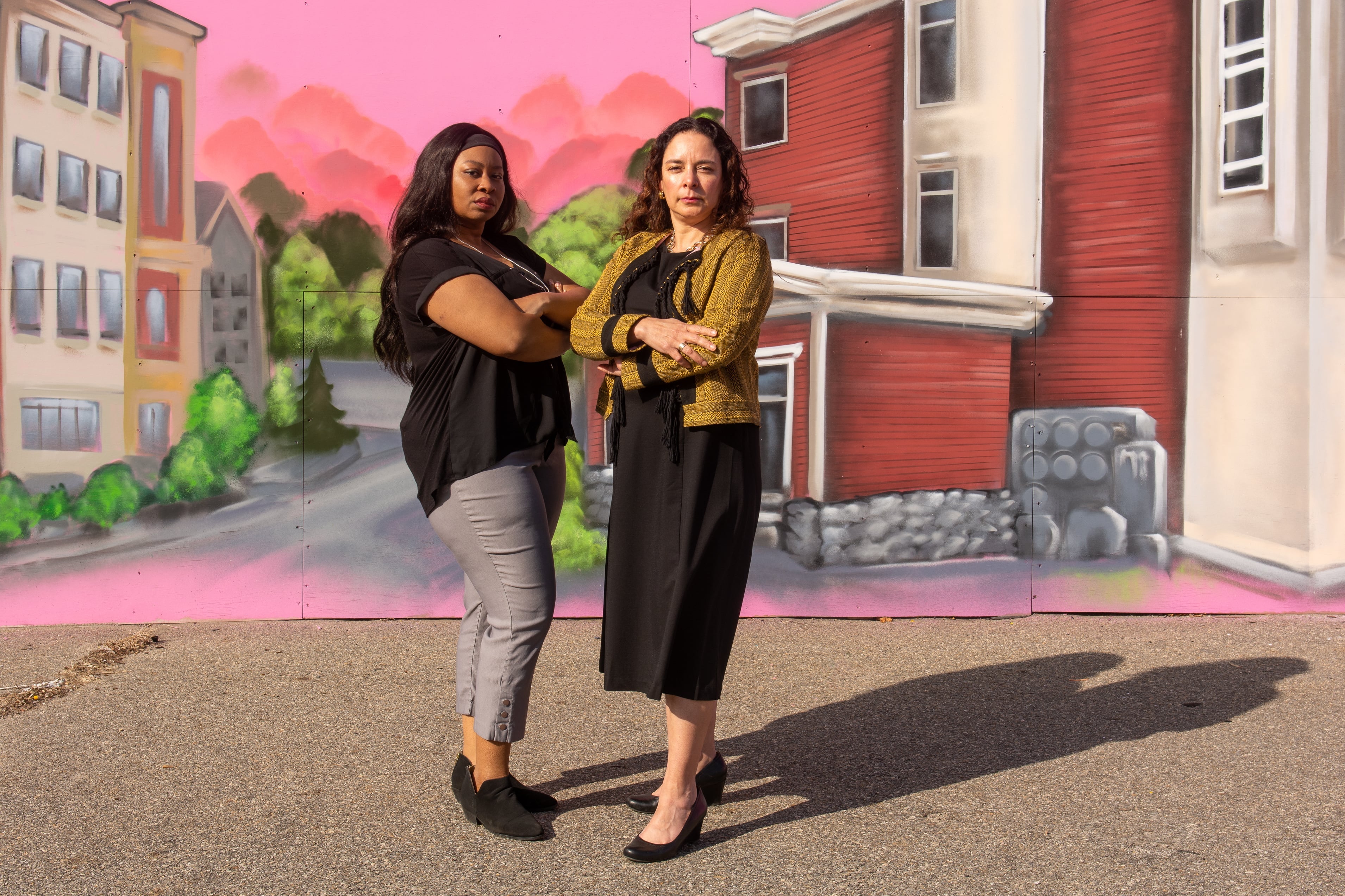 Two women stand in front of a pink mural