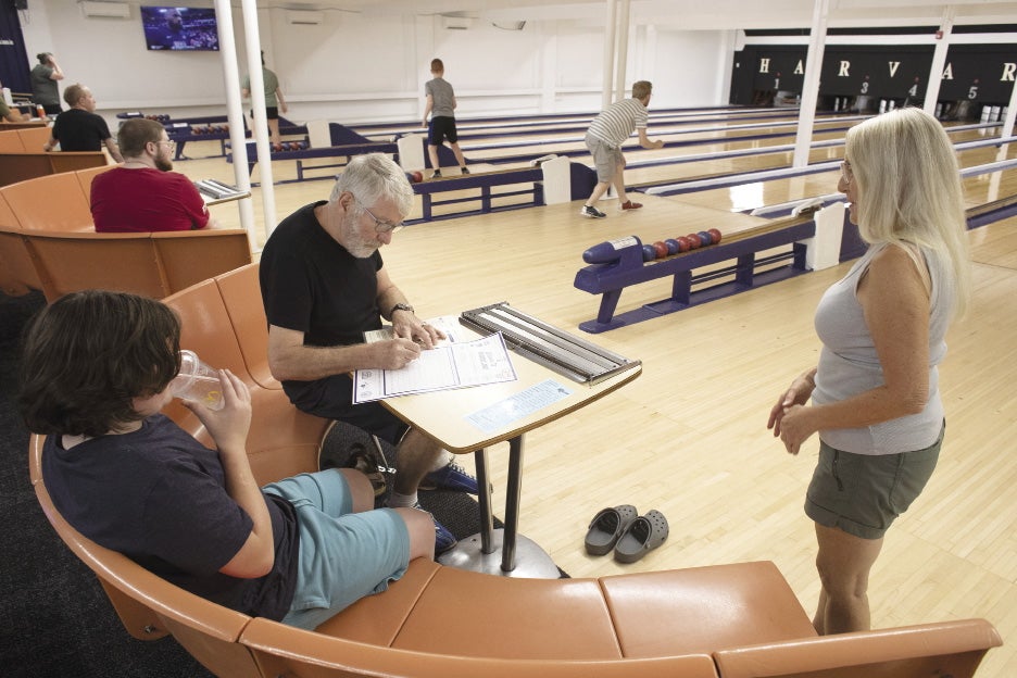 A group of three people sit on a bench near a scorer's table at a bowling alley