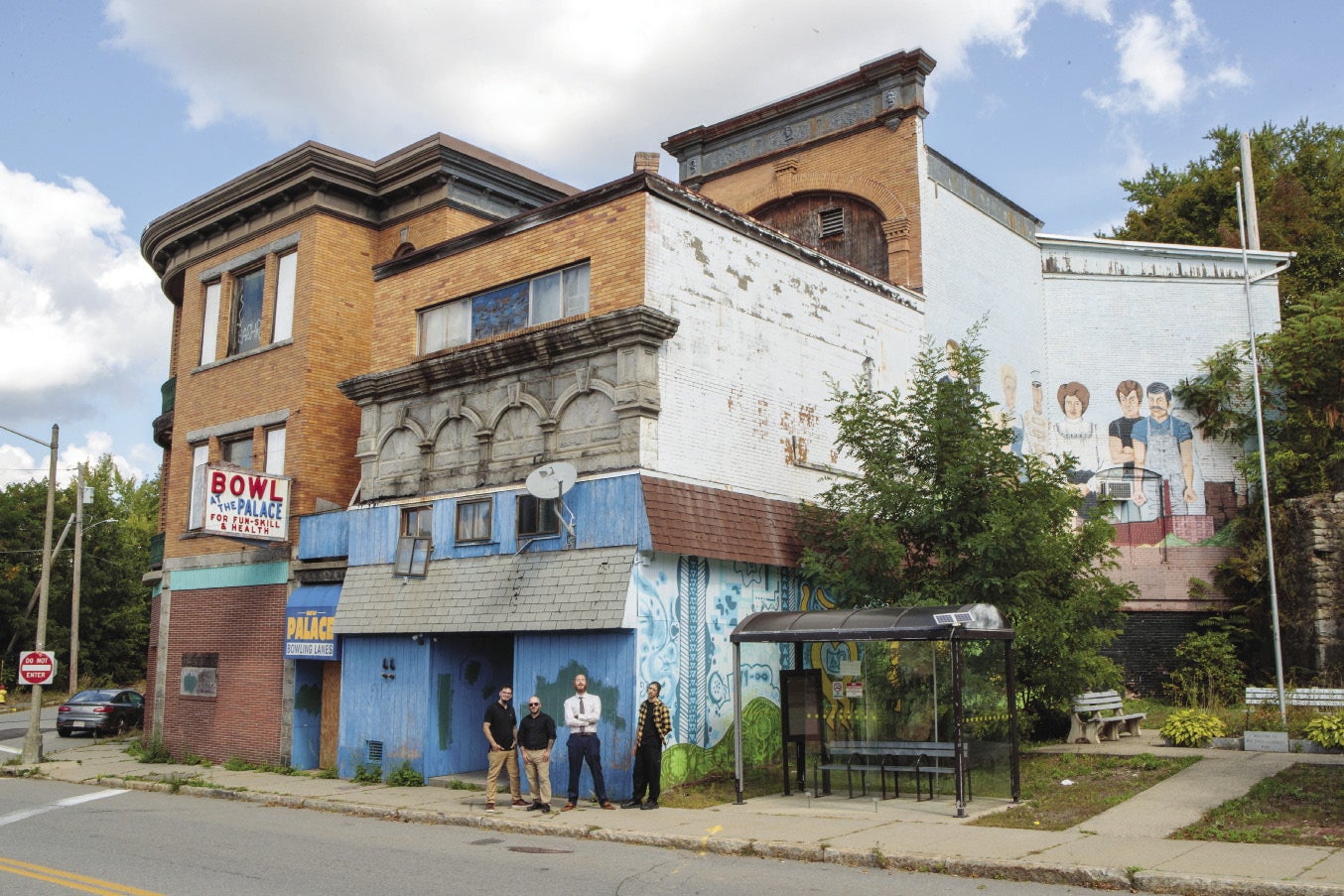 Four men stand in front of an older, rundown building.