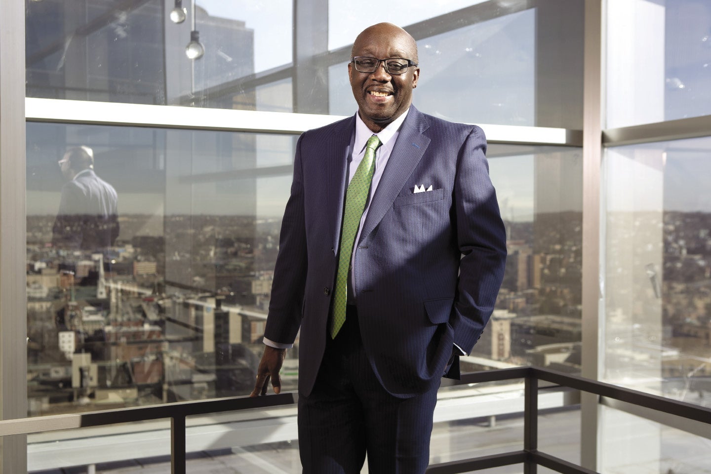 A man in a blue suit and green tie smiles at the camera in front of the Worcester skyline.