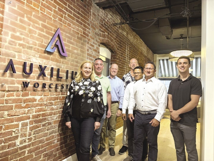 Seven people stand inside a hallway next to a brick wall with a sign reading "Auxilium Worcester"