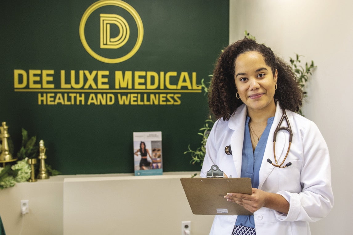 A woman with dark hair wears a white lab coat and stethoscope.
