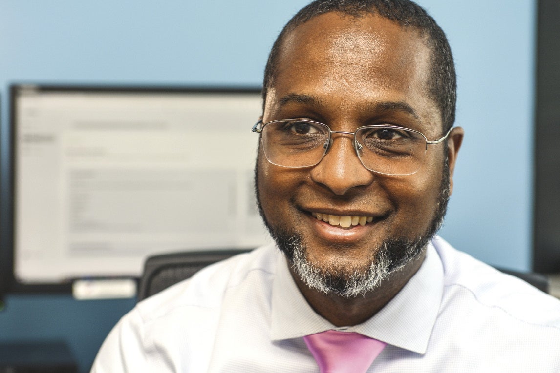 A man with glasses and a white button down and pink tie smiles for the camera.